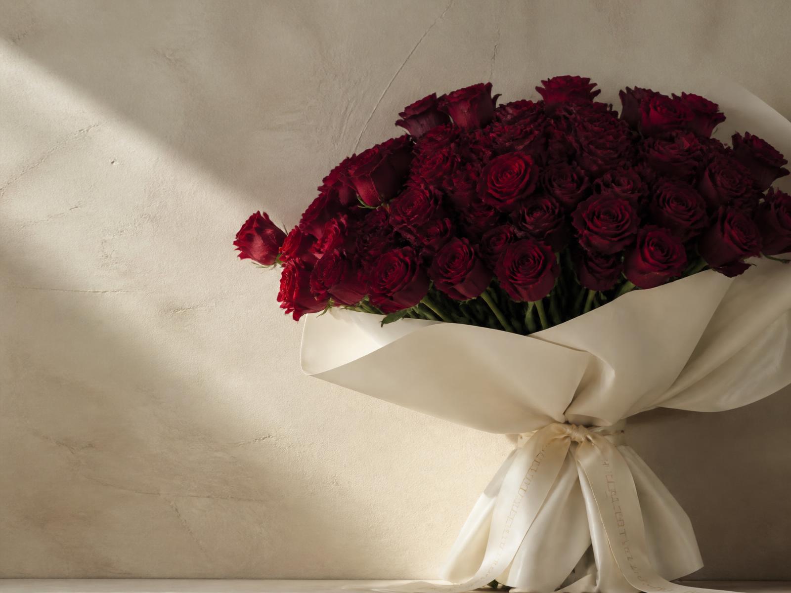 An oversized bouquet of deep burgundy roses wrapped in ivory paper and silk ribbon